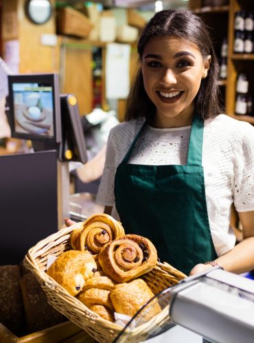 Female staff holding croissant in wicker basket at bread counter in supermarket